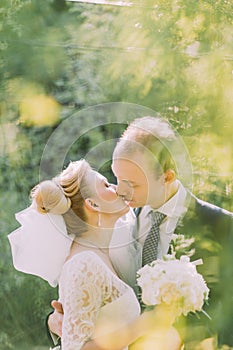 Portrait of beautiful young blonde bride and happy groom kissing on their wedding day outdoors