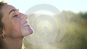 Portrait of a beautiful young blonde girl, under light summer rain, in the sun rays, on a green meadow. The girl smiles