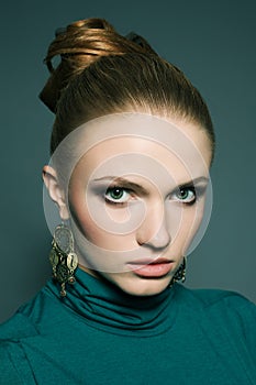 Portrait of a beautiful young blonde model wearing green blue dress and ethnic earrings over green blue background. Perfect