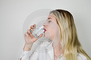 Portrait of a beautiful young blonde woman drinking a glass of water