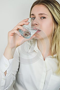 Portrait of a beautiful young blonde woman drinking a glass of water and looking at the camera