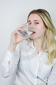 Portrait of a beautiful young blonde woman drinking a glass of water and looking at the camera
