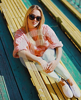 Portrait beautiful young blonde woman sitting on bench in a city park