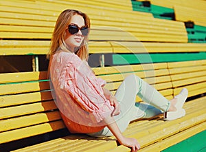 Portrait beautiful young blonde woman sitting on bench in a city park