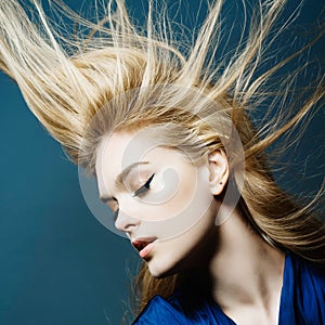 Portrait of a beautiful young blonde woman in studio on a blue background with developing hair