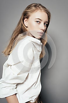 Portrait of a beautiful young blonde woman in a white shirt in the studio on a gray background