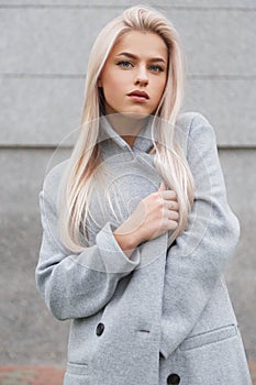 Portrait of a beautiful young blondhair woman in grey coat. Street fashion look