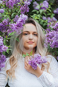 Portrait of beautiful young blue-eyed blonde woman near blooming lilac. Spring