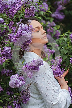 Portrait of beautiful young blue-eyed blonde woman near blooming lilac. Spring