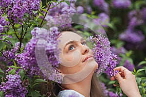 Portrait of beautiful young blue-eyed blonde woman near blooming lilac. Spring