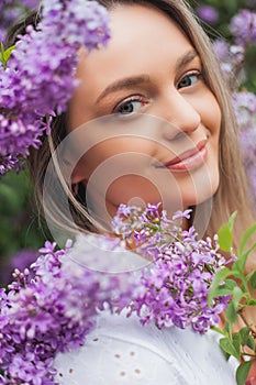 Portrait of beautiful young blue-eyed blonde woman near blooming lilac. Spring