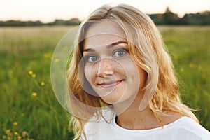 A portrait of beautiful young blue-eyed girl with light hair having charming smile and dimple on her face looking into camera stan