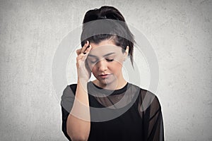 Portrait of beautiful young brunette with bare shoulders touching her temples feeling stress, on gray background