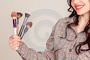 Portrait of a beautiful young brunette with long hair. girl makeup artist holds makeup brushes in her hands