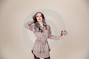 Portrait of a beautiful young brunette with long hair. girl makeup artist holds makeup brushes in her hands