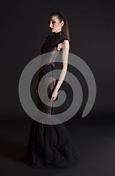 Portrait of beautiful young brunette woman in black dress against dark background, highlighted with red