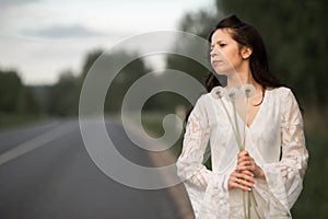 Portrait of  beautiful young brunette woman with dandelion flowers on the rural asphalt road