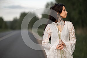 Portrait of  beautiful young brunette woman with dandelion flowers on the rural asphalt road