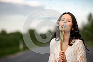 Portrait of  beautiful young brunette woman with dandelion flowers on the rural asphalt road