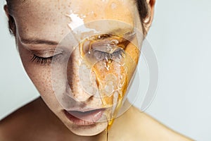 Portrait of beautiful young brunette woman with freckles and honey on face with closed eyes and serious face, head down