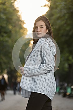 Portrait of beautiful young brunette woman in plaid shirt in the park. Student girl walks in the park