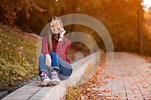 Portrait of beautiful young brunette woman in red shirt and jeans hiding eyes behind autumn leaves
