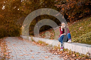 Portrait of beautiful young brunette woman in red shirt and jeans hiding eyes behind autumn leaves