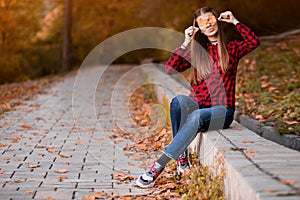 Portrait of beautiful young brunette woman in red shirt and jeans hiding eyes behind autumn leaves