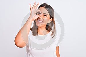 Portrait of beautiful and young brunette woman standing over isolated white background doing ok gesture with hand smiling, eye