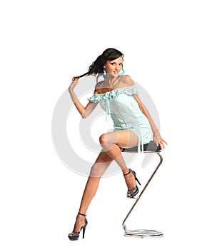 Portrait of beautiful young brunette woman in stylish dress and black shoes sitting on bar chair