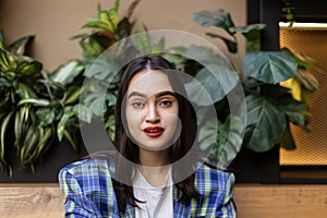 Portrait of beautiful young brunette woman wearing a checkered blazer against a backdrop of lush green foliage