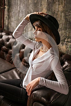 Portrait of beautiful young business woman in black hat and white shirt on leather sofa