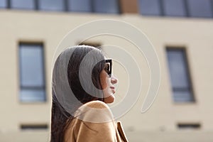 Portrait of beautiful young businesswoman outdoor over blurred street background. Profile of elegant brunette female, wears beige