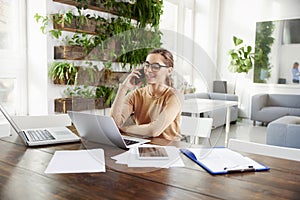 Attractive businesswoman making a call while sitting in front of laptop in the office and working