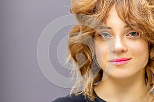 Portrait of a beautiful young caucasian red-haired woman with short wavy hairstyle smiling and looking at camera on dark