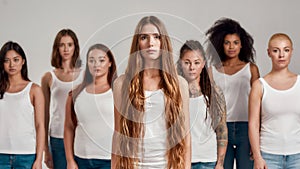 Portrait of beautiful young caucasian woman with long hair in white shirt looking at camera. Group of diverse women