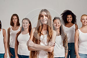 Portrait of beautiful young caucasian woman with long hair in white shirt smiling at camera. Group of diverse women