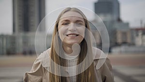 Portrait of beautiful young Caucasian woman standing in urban city on overcast day and smiling at camera. Positive