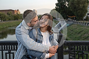 Portrait of beautiful young couple on the bridge. Guy gently embrace his beloved. Happy girl closed eyes. Romantic date