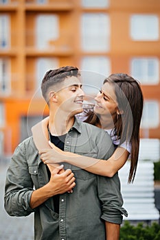 Portrait of beautiful young couple in casual clothes hugging, looking at camera and smiling in the street