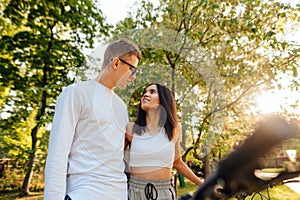 Portrait of a beautiful young couple in casual clothes standing in the autumn park, hugging and looking at each other with a smile