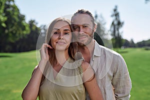 Portrait of beautiful young couple in casual wear smiling at camera, posing together outdoors in summer park