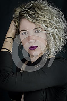 Portrait of a beautiful young curly blonde woman who adjusts her hair and looks seductively, with purple lipstick