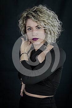 Portrait of a beautiful young curly blonde woman who adjusts her hair and looks seductively, with purple lipstick