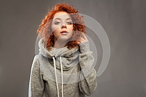 Portrait of a beautiful young curly-haired girl with fiery red hair looking at the camera on a gray background.