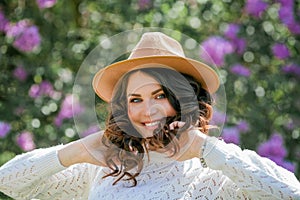 Portrait of beautiful young dark-haired woman with blue eyes in hat near the blooming. Happy model with curly hair. Spring