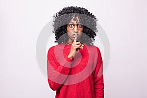 Portrait of beautiful young dark-skinned woman asking to keep silence holding finger on her lips isolated on white background