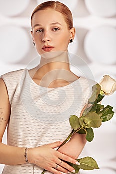 Portrait of a beautiful young disabled woman, born without an arm, holding a flower in her hands in a white dress