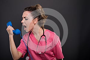 Portrait of beautiful young doctor yelling at telephone receiver photo