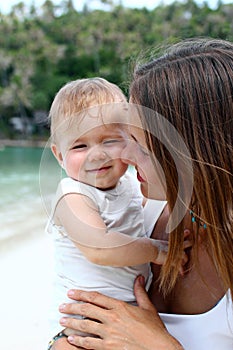 Portrait of beautiful young European mother hugging her little daughter on a background of tropical beach